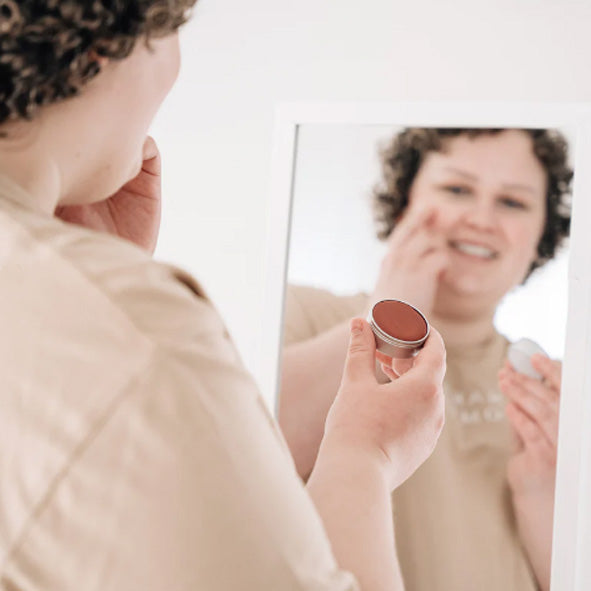Woman applying all natural handmade blush on her face.