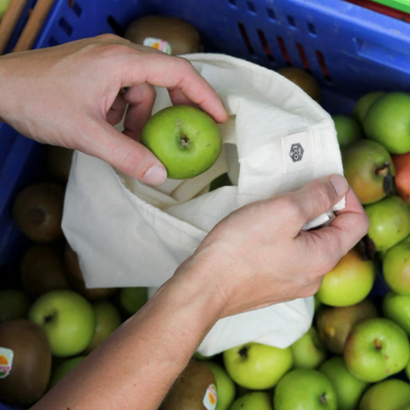 Load image into Gallery viewer, Person popping applies into a plastic-free reusable cotton produce bag.
