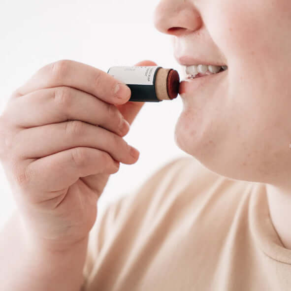 A woman applying a plastic-free lip tint in a cardboard tube.