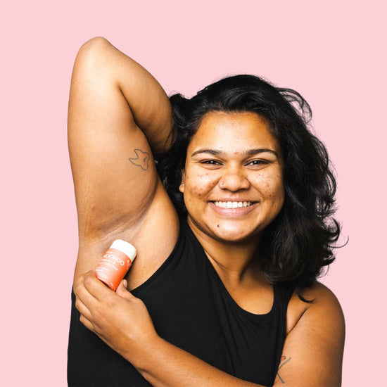 Woman using a plastic free tube of Woohoo Body's Urban all natural deodorant under her arm.