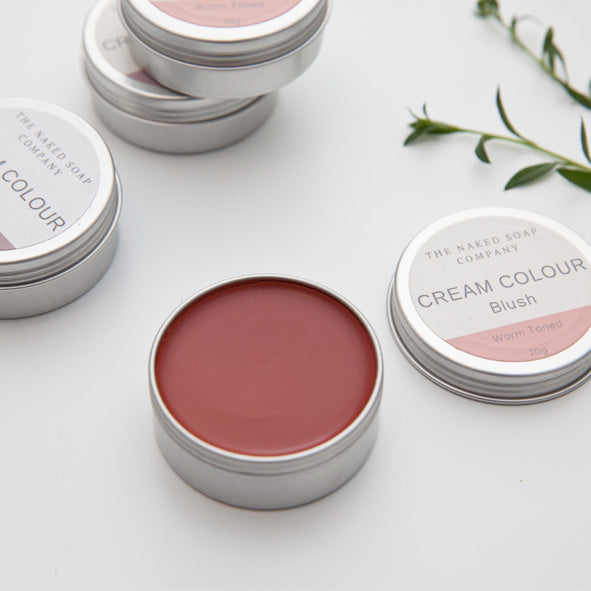 1 open tin of zero waste warm toned cream colour blush. In an aluminium tin. 3 tins in the background and on white. With some leaves scattered around.