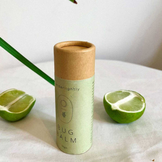 1 Recyclable cardboard tube of wanderlightly bug balm with 2 limes in the background. On a kitchen benchtop.