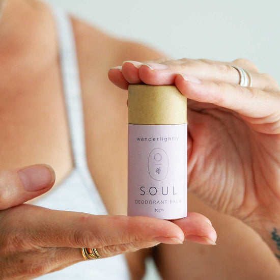 A Woman holding a smaller cardboard tube of Wanderlightly soul deodorant balm. Low waste store.