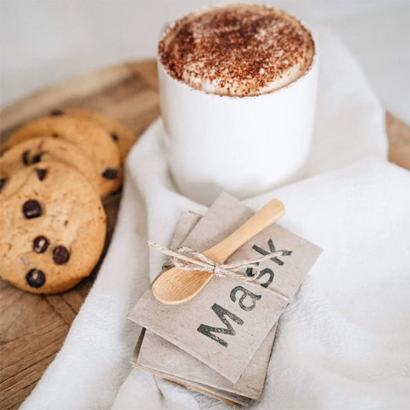 Load image into Gallery viewer, Set of 4 all-natural clay face masks with a wooden spoon by a cup of coffee and some chocolate cookies.
